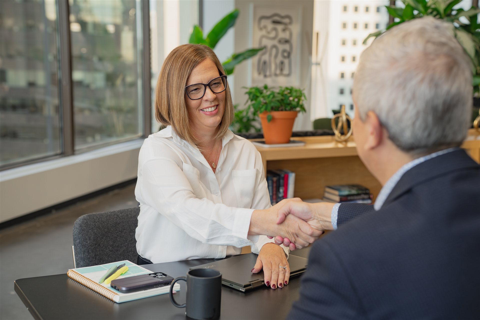 Two professionals smiling and shaking hands across an office desk